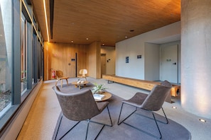 Una hall moderna con soffitto in legno, un'area salotto con due poltrone e un tavolo, e una panca lungo la parete.