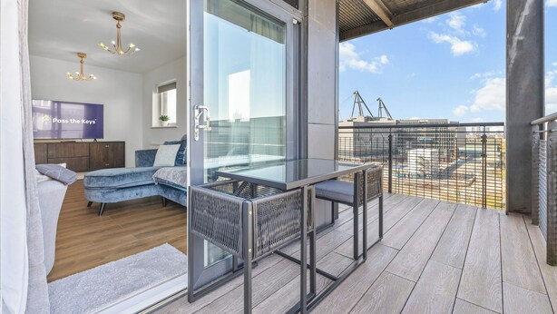 Ein modernes Zimmer mit Glastür und Zugang zu einem Balkon, einer Couch, einem Tisch und einem Fernsehbildschirm, der 'Pass the Keys' anzeigt.