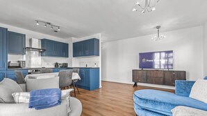 Ein modernes Wohnzimmer mit Sofa, Fernseher und Küchenzeile mit blauen Schränken und Herd.