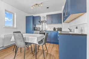 A modern kitchen with blue cabinets, a white dining table, and a window. - 6th Floor Balcony Flat Walk To Coop Arena & Etihad - Pass the Keys (Manchester)
