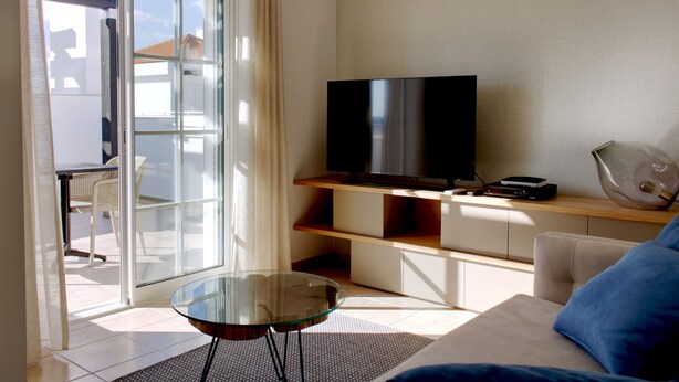 Uma sala de estar moderna com uma mesa de vidro, um sofá, uma televisão e uma porta de correr envidraçada que dá para uma área externa.
