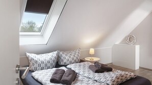 Un dormitorio con tragaluces, una cama con ropa de cama estampada, una lámpara de noche y una pequeña decoración en la pared.