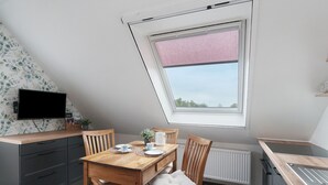 Un comedor con una mesa de madera, sillas, un televisor y una ventana con persiana rosa.