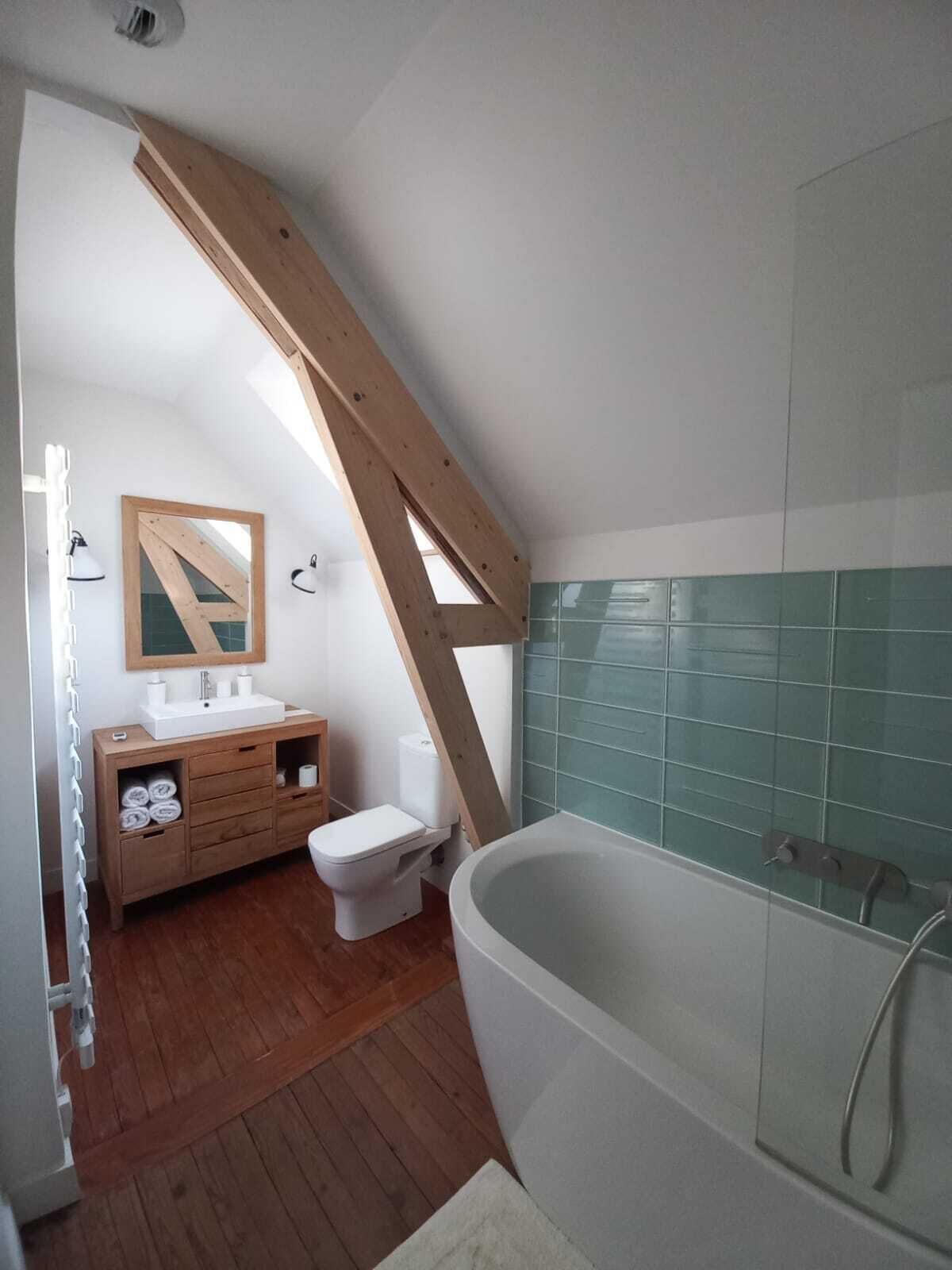 A bathroom with a wooden ceiling, a white bathtub, a toilet, and a vanity with a mirror.