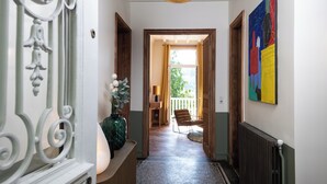 A hallway with a wooden door, a chair, a vase with flowers, and a colorful painting on the wall. - Villa Eliane (Étretat)