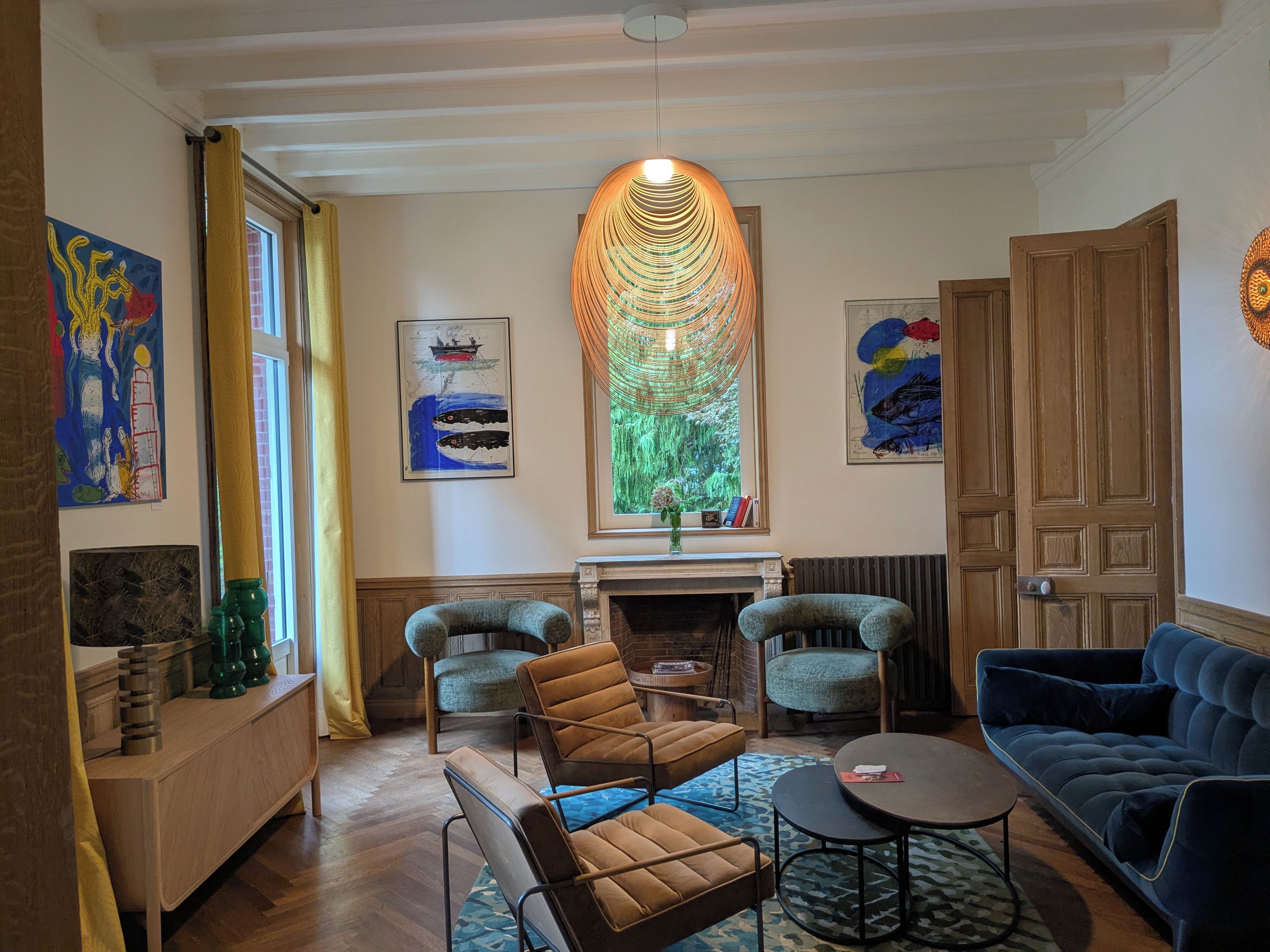 A room with a fireplace, two armchairs, a sofa, and artwork on the walls.