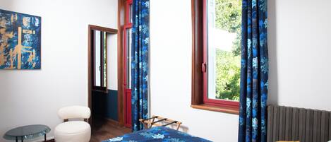 Une chambre à coucher avec un lit, une petite table, une chaise, un radiateur et une fenêtre avec des rideaux.