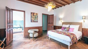 A bedroom with a wooden ceiling, a bed with a floral bedspread, a chair, and a painting on the wall. - Villa Eliane (Étretat)
