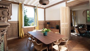 A spacious room with a large wooden dining table, chairs, a vase with flowers, and a view of the outdoors through a window. - Villa Eliane (Étretat)