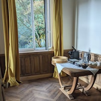 A room with a wooden table, a coffee maker, a kettle, and a window with curtains.