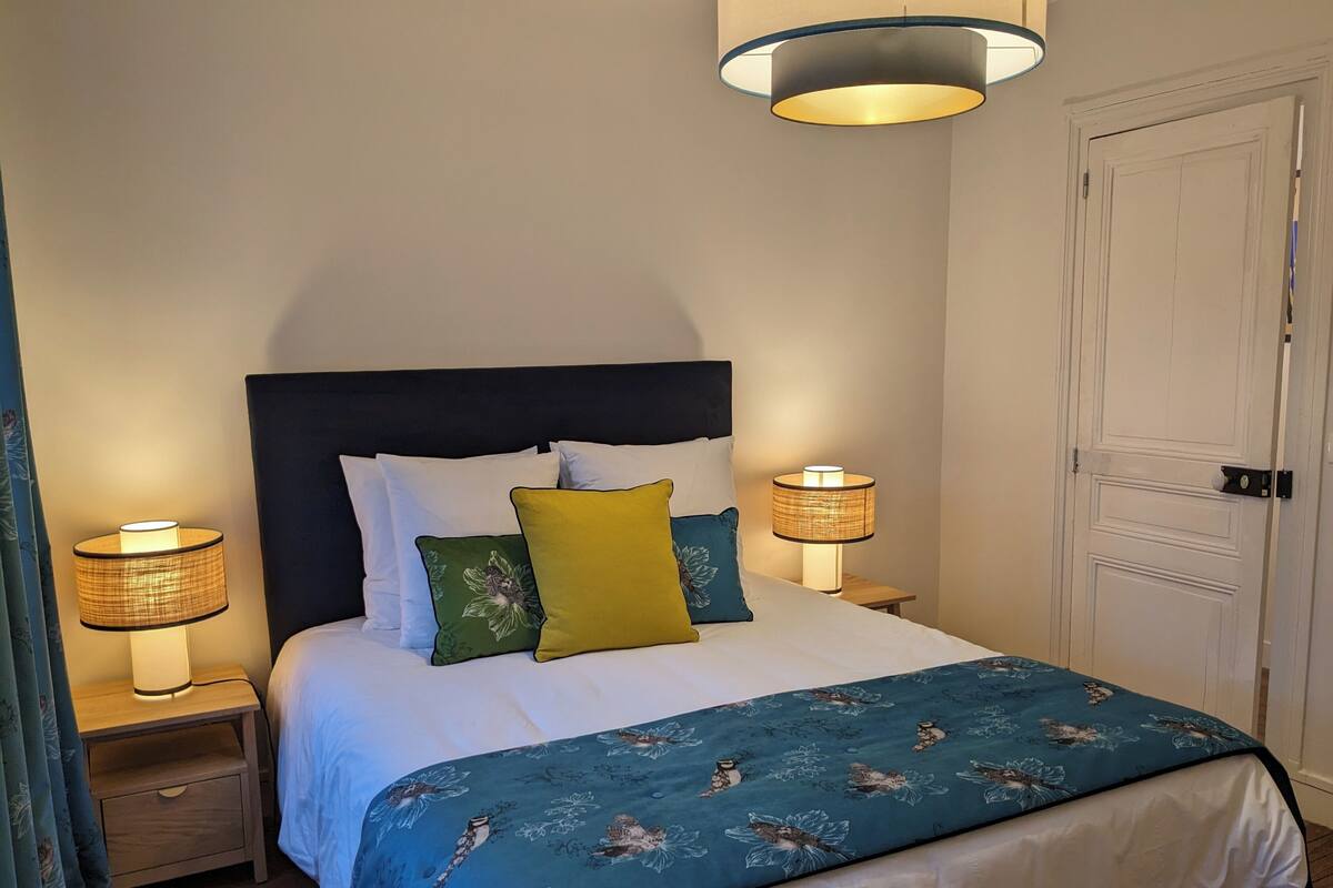 Un dormitorio con una cama, dos lámparas de noche, una mesita de noche, una puerta y una ventana con cortinas.