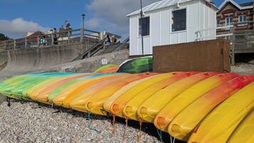 A row of colorful kayaks lined up on a pebbled beach, a lifeguard tower, and a wooden structure.