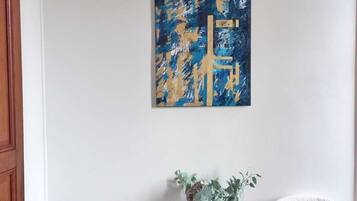 A room with two white chairs, a small table with a vase, and a blue abstract painting on the wall.