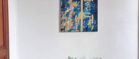 Una habitación con dos sillas blancas, una mesa pequeña con un florero y un cuadro abstracto azul en la pared.