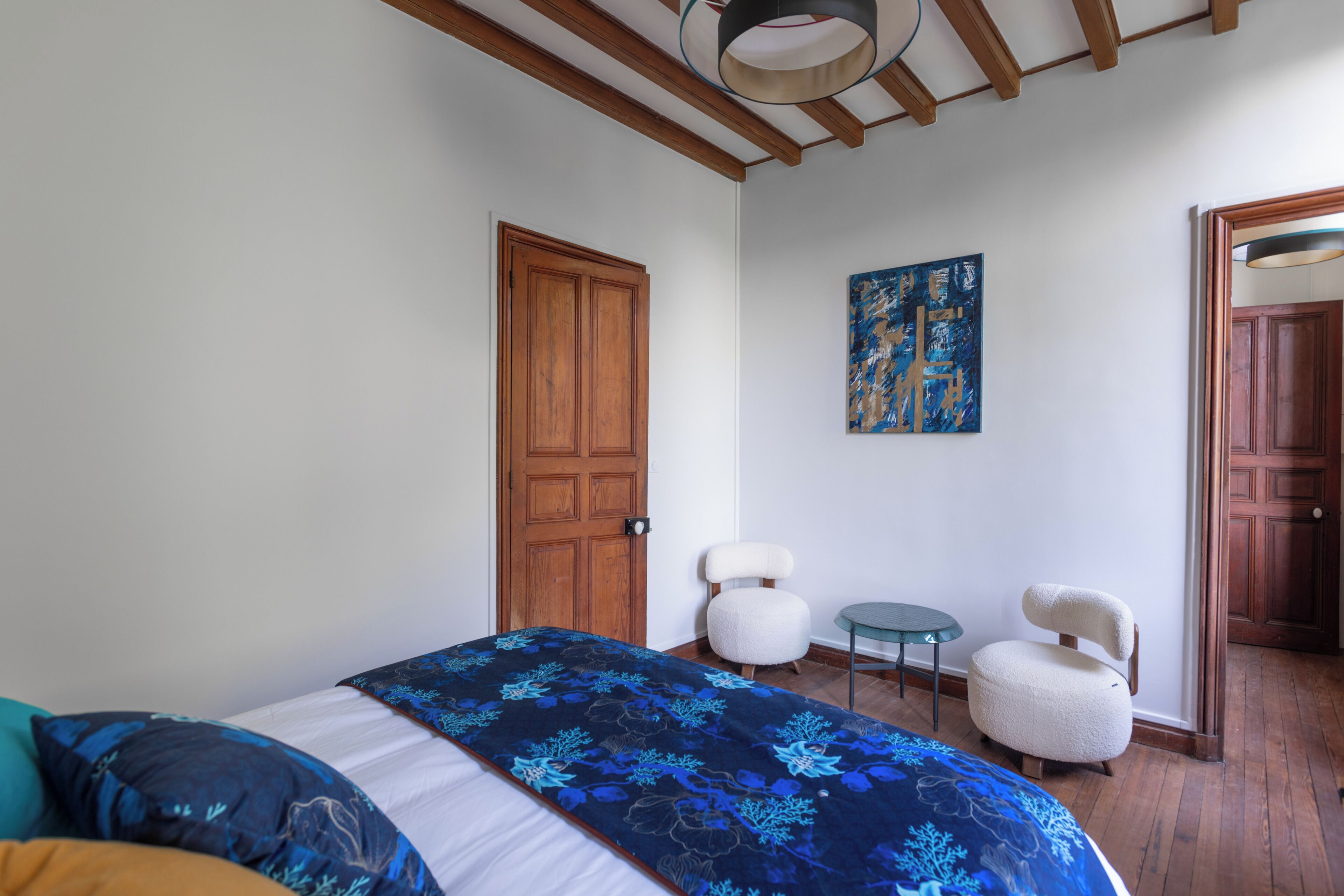 Een slaapkamer met een bed, twee stoelen, een klein tafeltje en een houten deur.