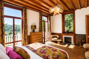 Quarto com cama, penteadeira, cadeira, lareira e grandes janelas.
