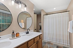 A bathroom with a double sink, a large mirror, a shower curtain, and a light fixture above the mirror. - Epic Views•Hot Tub•Game Room•Private•Near PF, Gatlinburg & GSMNP (Sevierville)