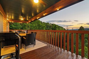 A wooden deck with a grill, wicker furniture, and a view of a forested landscape. - Epic Views•Hot Tub•Game Room•Private•Near PF, Gatlinburg & GSMNP (Sevierville)