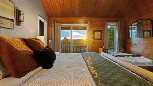 Quarto de cabana de madeira com cama, janela com cortinas, vista para o exterior e uma banheira.