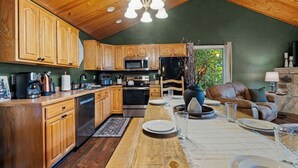 Cozinha com armários de madeira, eletrodomésticos de aço inoxidável e um espaço de jantar com mesa posta para quatro pessoas.