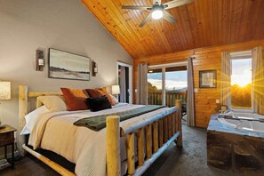 Ein Schlafzimmer einer Holzhütte mit Bett, Deckenventilator, Blick ins Freie und Whirlpool.