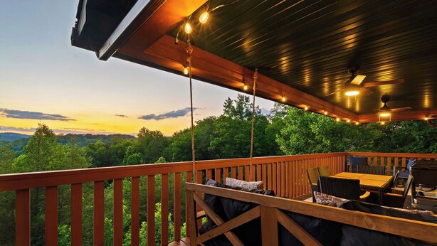 Um deck de madeira com mesa e cadeiras, com vista para uma paisagem arborizada.