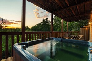 Ein Whirlpool auf einer Holzterrasse mit Blick auf Bäume und einen Sonnenuntergang.