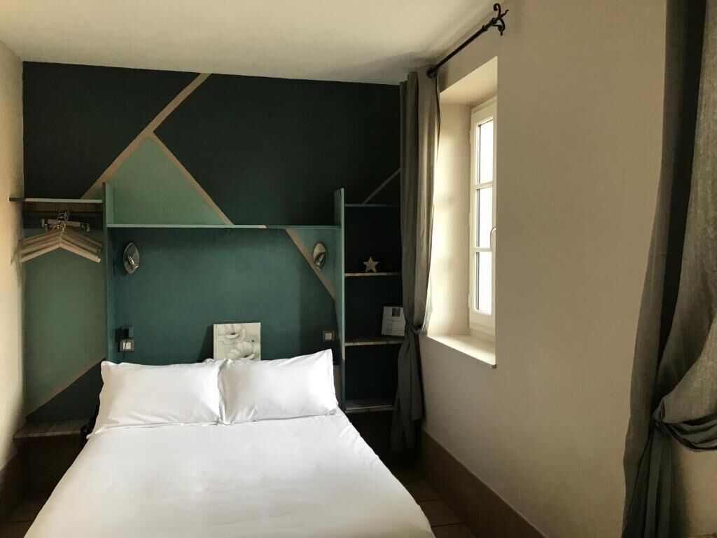Una cama con sábanas blancas, una pared de color aguamarina y una ventana con cortinas.