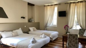A hotel room with two beds, a desk, a chair, a TV, and a window with curtains.