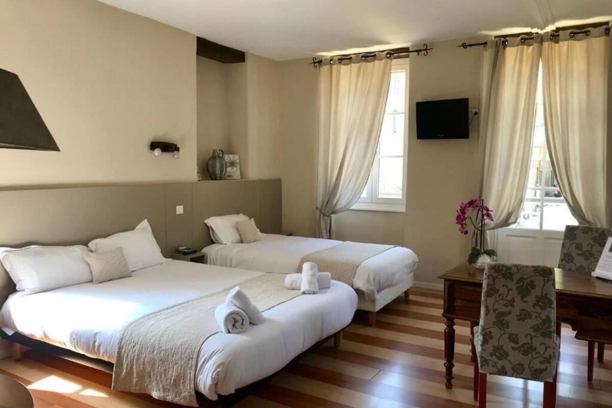 A hotel room with two beds, a desk, a chair, a TV, and a window with curtains.
