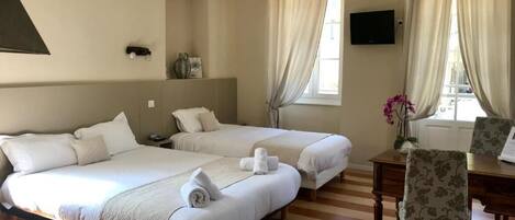 Habitación de hotel con dos camas, un escritorio, una silla, un televisor y una ventana con cortinas.