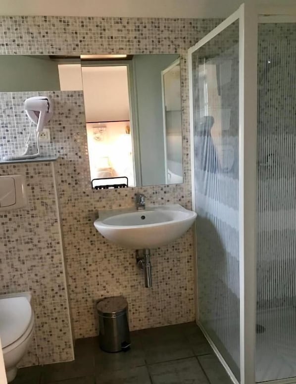A bathroom with a tiled backsplash, a sink, a toilet, a mirror, and a shower enclosure. - HOTEL DES BAINS (Figeac)