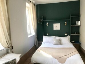 A neatly arranged bedroom with a bed, bedside tables, a nightstand, and a window with curtains. - HOTEL DES BAINS (Figeac)