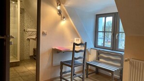 A room with a sloped ceiling, a window with a view, a chair, a bench, and a shower area.