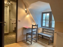 Una habitación con techo inclinado, una ventana con vistas, una silla, un banco y una zona de ducha.