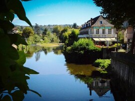 Un hotel junto a un río tranquilo, con vistas a la vegetación y colinas circundantes.