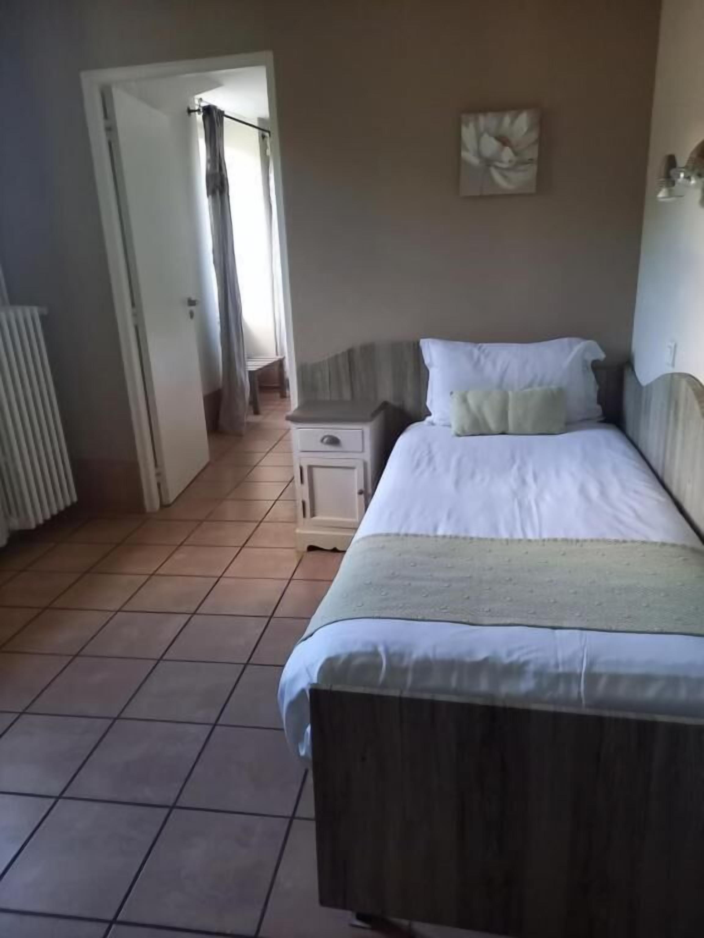 A bedroom with a bed, a nightstand, a radiator, and a door leading to another room.