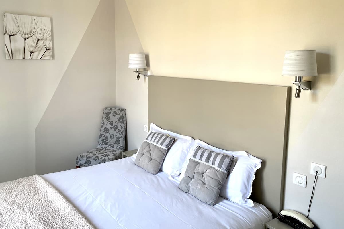 A hotel room with a bed, a chair, a lamp, and a painting on the wall.