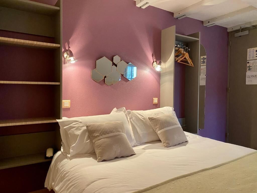 Een slaapkamer met een bed, een wandlamp en een deur met kapstok.