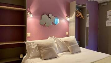 Een slaapkamer met een bed, een wandlamp en een deur met kapstok.