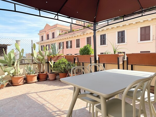 Un patio exterior con una mesa y sillas, rodeado de plantas en macetas y una valla.