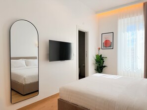 Habitación de hotel con cama, televisor, espejo, puerta, planta y ventana con cortinas.