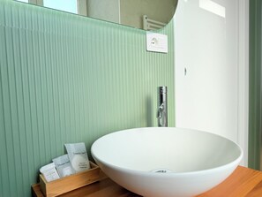 Un baño con un lavamanos grande de color blanco, una bandeja de madera con artículos de aseo y una pared verde con textura.