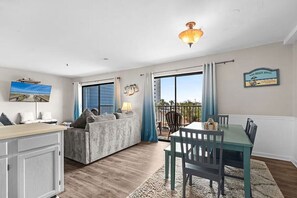 Een woonkamer met een bank, een eettafel met stoelen, een aan de muur bevestigde televisie en een balkon met uitzicht.