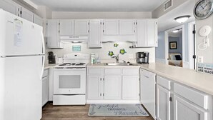 A kitchen with white cabinets, a stove, a sink, and a clock on the wall.