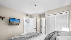 A bedroom with a bed, a television mounted on the wall, and a door leading to another room.