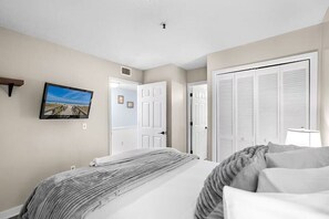 A bedroom with a bed, a television mounted on the wall, and a door leading to another room. - Myrtle's Finest (Myrtle Beach)