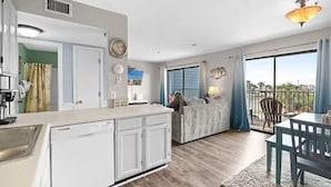A kitchen with a dishwasher, a dining area with a table and chairs, a sofa, and a view of the outdoors.