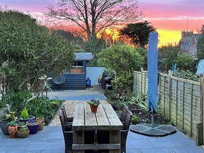 Une terrasse avec une table et des chaises en bois, entourée de plantes en pot et d’un jardin.