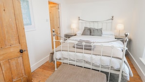 Een slaapkamer met een wit metalen bed, twee nachtkastjes met lampen, een houten deur en een klein vloerkleed.